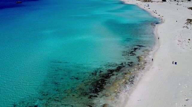 Drone footage of the turquoise shoreline and crystal-clear waters at Simos Beach, Elafonisos, Greece, showcasing white sand and vibrant Mediterranean colours.