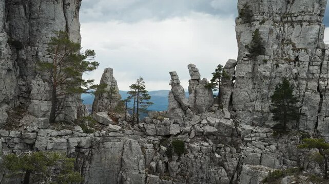 A detail of a rock formation at the summit of Cadi&egrave;res de Brandis in France. The rugged, massive rocks are piled on top of one another. Green trees and shrubs grow among them. Rocks are scattered.