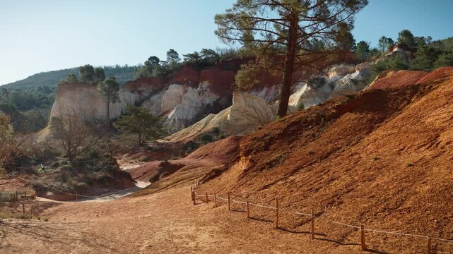 View of the deserted and expansive ochre-colored rock landscape of Rustrel in France. The colorful, red landscape is bathed in the morning sun.