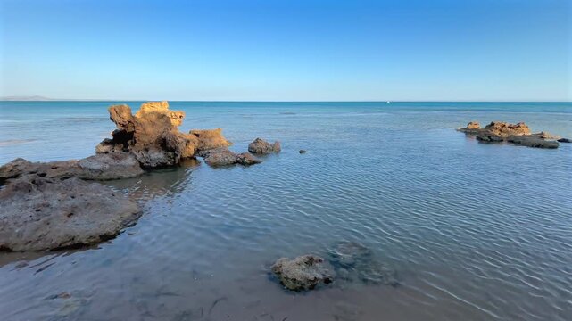 Calm Mediterranean Sea washing over a rocky coastline in Sicily on a sunny summer day. Scenic coastal landscape with crystal clear water and natural rock formations.
