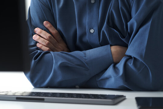 Businessman thinking about problem while sitting at computer with crossed arms in office. Man and desktop computer keyboard.