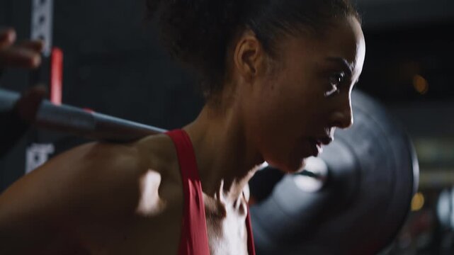 Muscular african american woman sweating during a weightlifting workout session. Intense close up of a focused female athlete exercising with a barbell in a dark and gritty functional gym