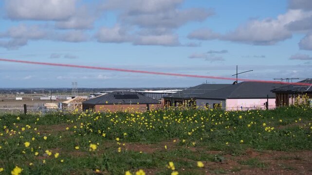 Vacant residential land covered in wildflowers blooming across a grassy hill in Truganina, Melbourne Australia. Newly framed homes under construction sit along the urban fringe