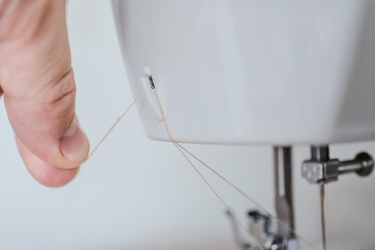Male hands preparing sewing machine to stitch fabric at home Macro detail of thread guidance system in domestic sewing machine ready for sewing process