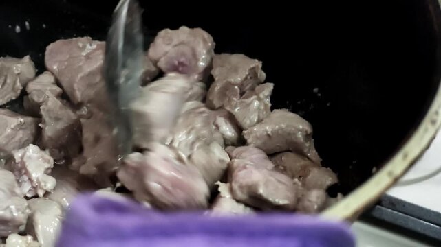 Close up scene shows irregular beef chunks browning in dark skillet with bubbling fat, rendered juices, pink centers, seared texture, and caramelized surfaces for rich home kitchen cooking action