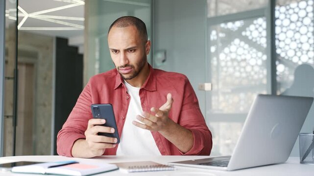Worried businessman having problems with software or service on smartphone mobile phone sitting at workplace in business office. Frustrated disappointed worker complains about bad internet connection