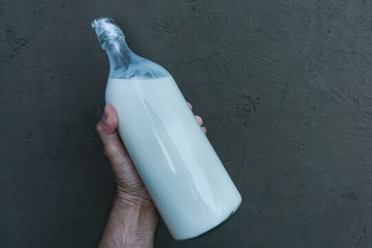 masculine hairy man hand holding bottle of milk on dark black concrete cement wall for natural daily product for men banner advertisement 