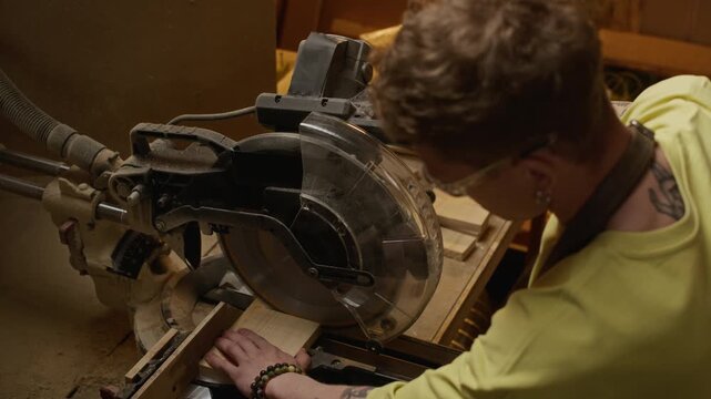 Young adult Caucasian male carpenter cutting wooden block with miter saw and inspecting finished pieces in workshop. Video is ideal for carpentry business promotions or DIY woodworking tutorials