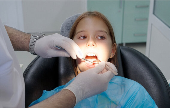 Pediatric dentist examining teeth of a brave girl sitting in dental chair