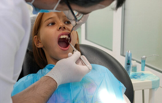 Pediatric dentist examining teeth of a brave girl sitting in dental chair