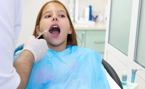 Pediatric dentist inserting saliva ejector for young girl during treatment