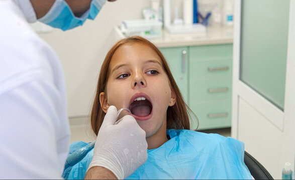 Pediatric dentist inserting saliva ejector for young girl during treatment