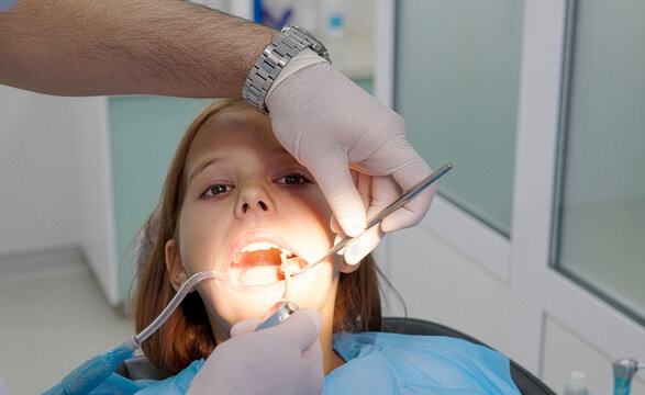 A pediatric dentist treats the teeth of a little girl sitting in the dental chair.