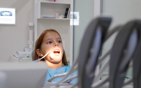 Pediatric dentist inserting saliva ejector for young girl during treatment