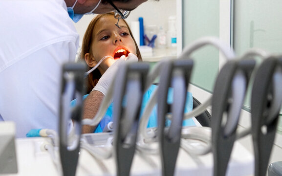 A pediatric dentist treats the teeth of a little girl sitting in the dental chair.