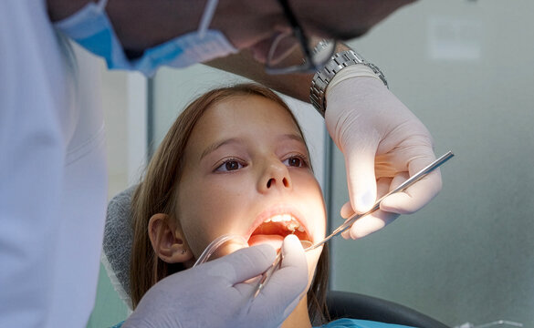 Pediatric dentist examining teeth with mirror and probe for young girl