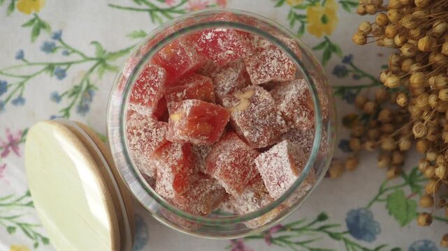 Turkish delight sweet cubes in glass jar and dried flax plant on floral background close up