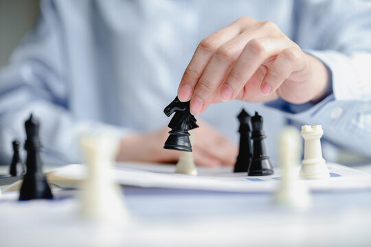 Close up hand of businesswoman moving black knight chess piece on desk for corporate strategy planning and leadership management in office. Concept of business success and tactic under pressure.