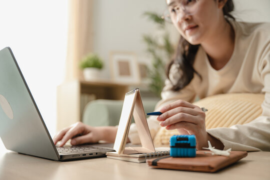 Close up female hands pointing pen on desk calendar searching vacation destination on laptop. Concept of travel planning, online travel agency booking, and personal itinerary planning.