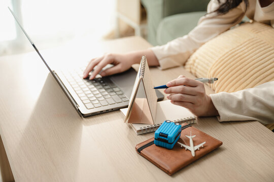 Female hands pointing pen on desk calendar searching vacation destination on laptop. Concept of travel planning, online travel agency booking, and personal itinerary planning.