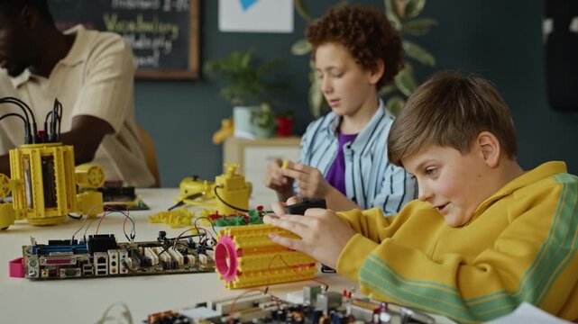 Caucasian teenager assembling robotic parts during STEM class with classmates and African American teacher in background. Perfect for promoting modern education and robotics programs