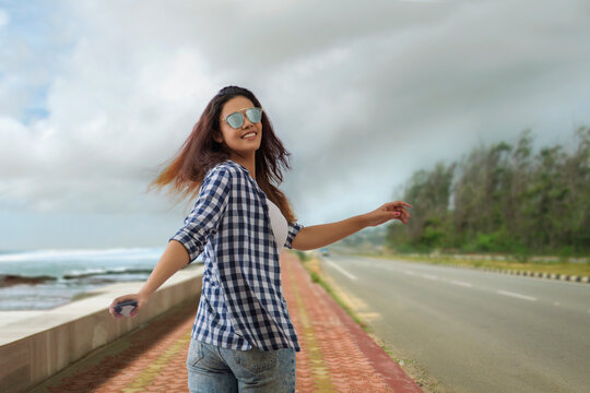 Woman walking on a beach side road holding a mobile phone