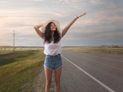 Woman in hat standing on highway waving her hand to stop vehicle for a lift