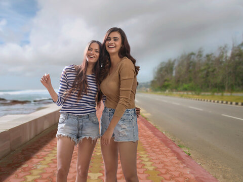Two women standing together on a footpath beside sea