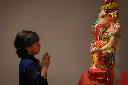 Kid praying with hands joined and eyes closed in front of Ganpati Idol.