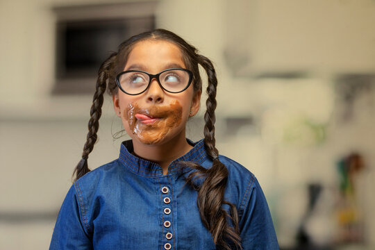 Girl wearing eyeglasses licking the chocolate around her mouth looking up