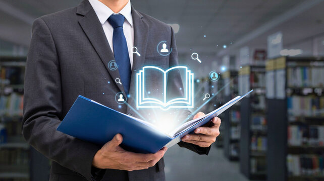 Professional businessman holding a luminous digital book icon illustrating modern online education and corporate knowledge management