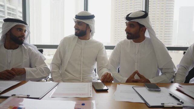 Arab businessmen wearing emirati kandura meeting in office for business deal - Corporate business group of middle-eastern people working in an international company in middle east