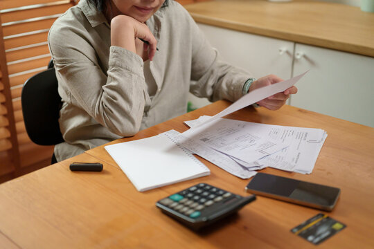 Woman reviews household bills with a calculator and receipts, managing personal finances, budgeting, and monthly expenses for smarter financial planning at home.