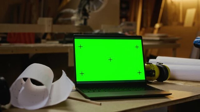 Laptop with green screen displaying tracking markers placed on workbench in carpentry workshop next to blueprints. Footage is perfect for promoting digital design software for woodworkers