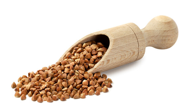 Raw buckwheat pouring from a wooden scoop on a white background. Isolated