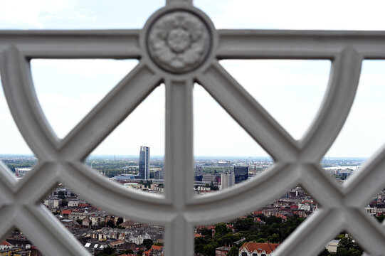 famous tall building seen through a circular hole of a cast iron fence. view from the Citadel in Budapest, Hungary. the tallest glass office building of a large oil company. residential building roofs