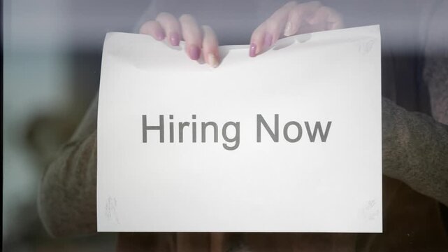 Business owner tearing down hiring now sign from store window.