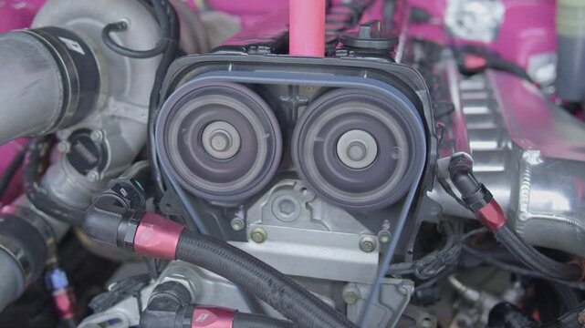 Slow-motion close-up of adjustable cam gears, timing belt, and high-performance engine bay components of a tuned sports car.