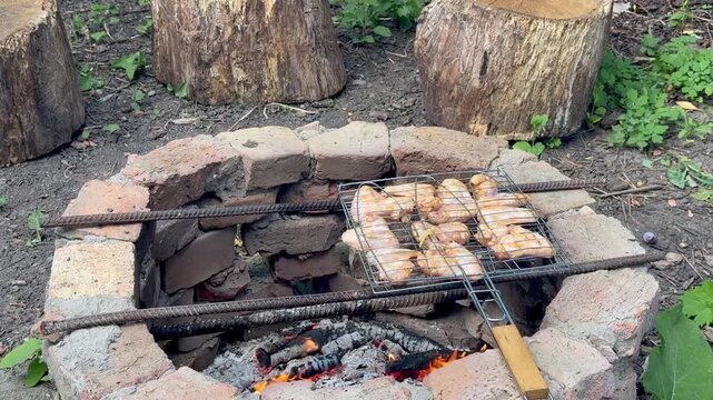 Chicken wings grilling on wire rack over open brick fire pit outdoors