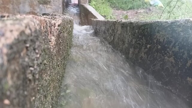 Detailed motion footage showing violent water rushing downstream over rocks in a riverbed during a sudden downpour.