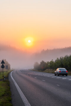 Car driving on foggy road at sunrise in morning
