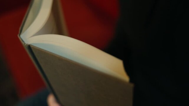 Close-up of an open book with pages being turned in warm soft light, creating a calm reading, study and literature atmosphere.