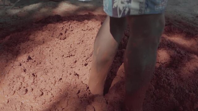 Barefoot indigenous people stomping and mixing clay with their feet. A traditional method of preparing mud for natural building in Brazil