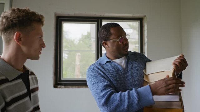 African American male designer showing color swatches to Caucasian young adult male client at renovation site. Footage is ideal for interior design services and home improvement marketing