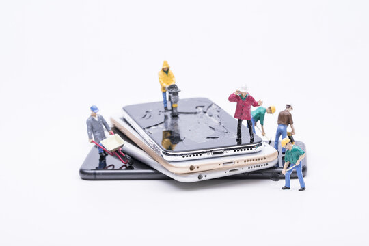 Miniature workers repairing damaged smartphones on white background