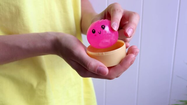 Close-up of hands opens package of pink dumpling shaped glitter squishy toy and then squeezing it during sensory play. Concept of stress relief, tactile activity, relaxation and emotional balance.