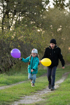 Children joyfully walking along a grassy path in a park during late afternoon, each holding colorful balloons while enjoying their time together