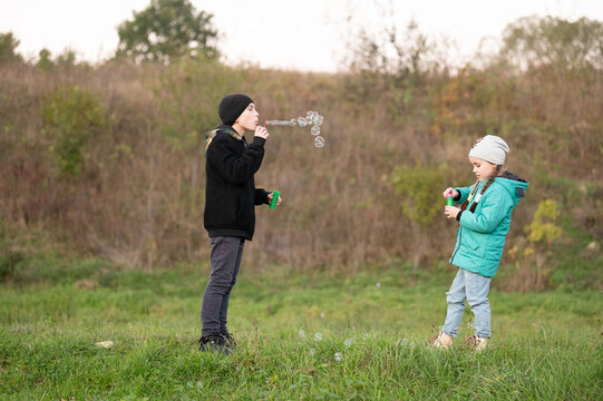 Children joyfully creating bubbles during a sunny afternoon in a tranquil field, surrounded by nature and laughter with smiles on their faces