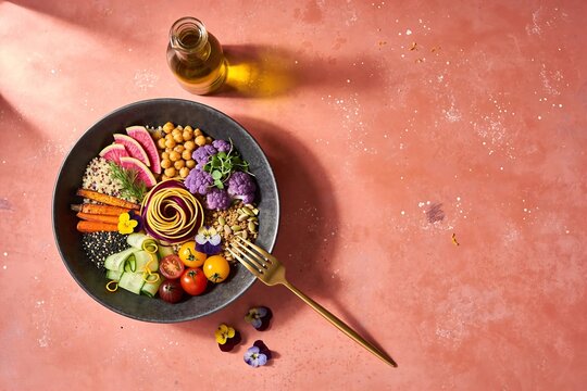 Mediterranean grain salad bowl with quinoa radish carrots tomatoes on coral pink surface with space for copy