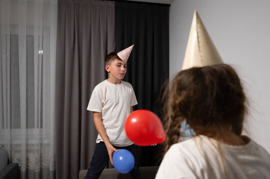 Children celebrate a fun birthday party indoors with balloons, party hats, and joyful expressions during the afternoon in a cozy living room